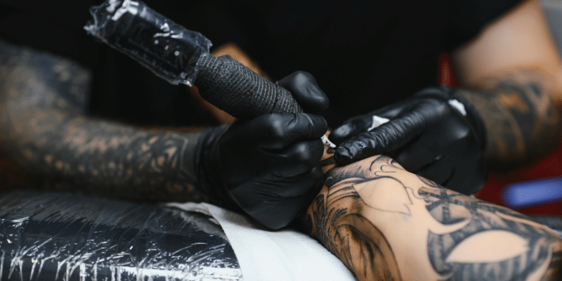 Tattoo artist at work on clients arm - Essential First Aid Supplies for Tattoo Studios